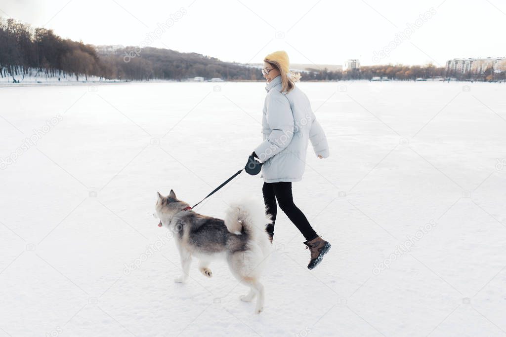 Happy young girl playing with siberian husky dog in winter park