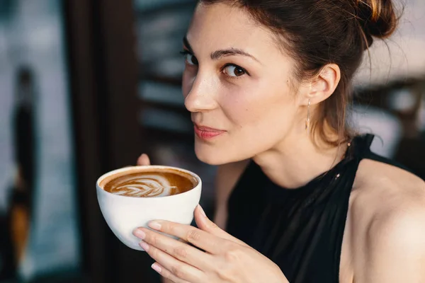 Raffinierte Frau genießt Cappuccino oder Latte auf einem lebendigen, farbenfrohen Hintergrund drinnen. — Stockfoto