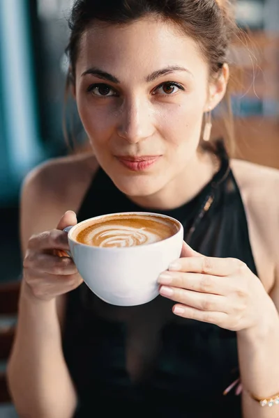 Raffinierte Frau genießt Cappuccino oder Latte auf einem lebendigen, farbenfrohen Hintergrund drinnen. — Stockfoto