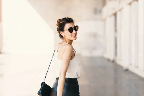 Улыбающаяся молодая женщина в солнцезащитных очках, глядя через плечо во время прогулки — стоковое фото