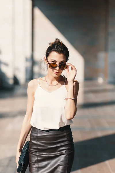 Mujer de negocios refinada sosteniendo gafas de sol de moda mirando por encima de ellos en un fondo borroso — Foto de Stock