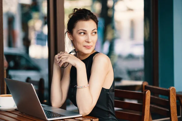 Mulher de negócios refinada em óculos, sentada à mesa no café trabalhando no laptop — Fotografia de Stock