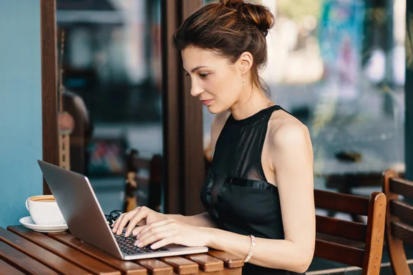 Raffinata donna d'affari in occhiali, seduta a tavola in un caffè che lavora al computer portatile — Foto Stock