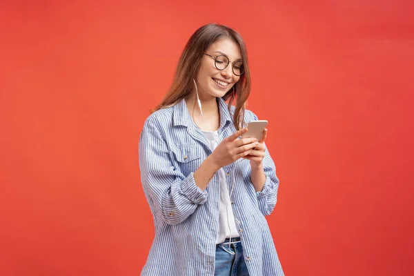 Menina sorridente em roupas casuais e fones de ouvido olhando para tela do telefone — Fotografia de Stock
