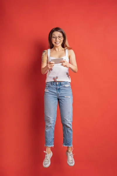 Surprised young woman always on mobile on red background