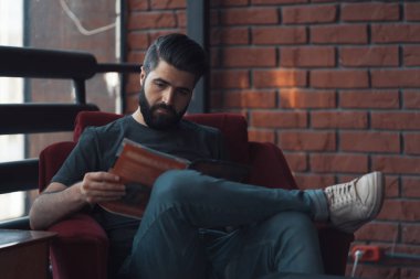 Portrait handsome bearded man wearing casual clothing, sitting in red chair modern loft studio