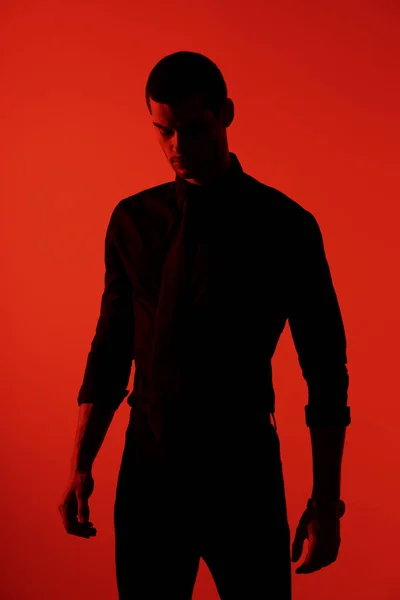 Silueta de un joven empresario guapo y seguro de sí mismo con camisa negra a la luz roja — Foto de Stock