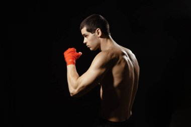 Sporcu boksör yan tekme pratiği yapıyor. Ellerinde kırmızı bandaj var. Siyah arka planda kaslı boksör. Spor konsepti.