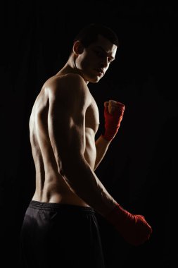 Boks duruşu yapan erkek boksörün portresi, omuzlarının üzerinden, siyah arka plana bakıyor..