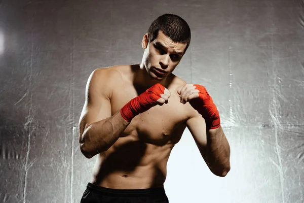 Athletic boxer punching with determination and precaution over silver background. Strength, attack and motion concept. Fit caucasian model in movement