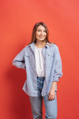 Kırmızı arka planda gülümseyen yüz ifadesiyle poz veren uzun saçlı güzel bir kadın manken.