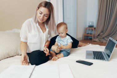 Çocuğuyla birlikte yatak odasında çalışan genç bir anne. Çoklu görev, serbest meslek ve annelik kavramı
