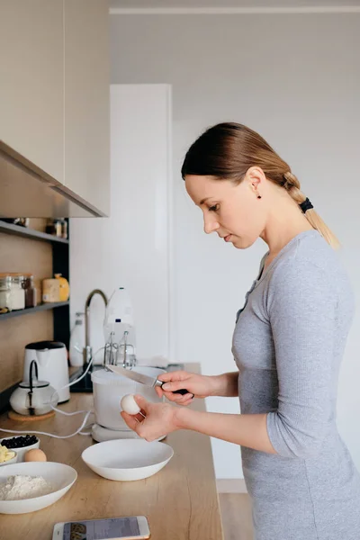 Vrouw breekt kippeneieren in een kom in de keuken. — Stockfoto