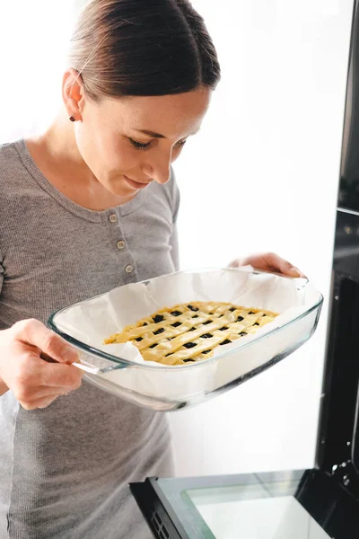 Jonge vrouw zet de zelfgemaakte taart in de oven — Stockfoto