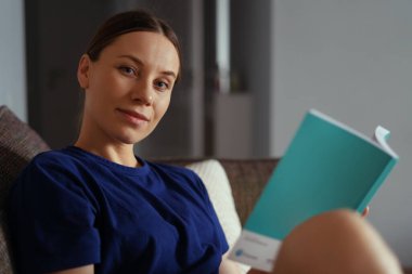 Çekici, pozitif kadın koltukta kitap okuyor.