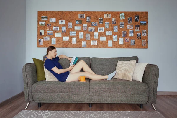 Atractiva mujer positiva leyendo un libro relajándose en el sofá — Foto de Stock