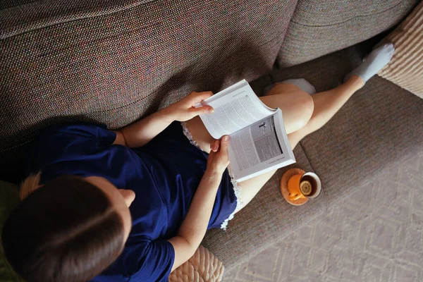 Atractiva mujer positiva leyendo un libro relajándose en el sofá —  Fotos de Stock