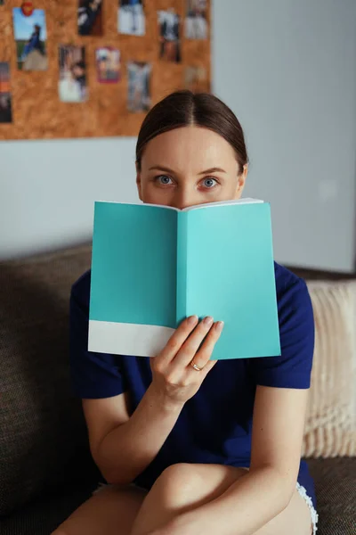 Attraktiv positiv kvinna läser en bok avkopplande på soffan — Stockfoto