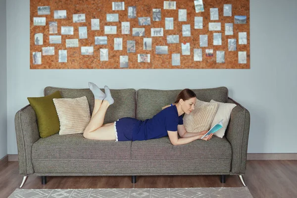 Atractiva mujer positiva leyendo un libro relajándose en el sofá — Foto de Stock