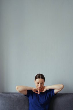 Oturma odasındaki kanepede dinlenen ve kollarını uzatan bir kadın.