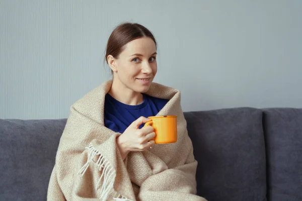 Mujer positiva disfrutando de una taza de té envuelta en una manta — Foto de Stock