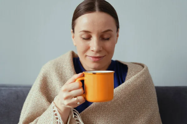 Mulher positiva desfrutando de uma xícara de chá envolto em um cobertor — Fotografia de Stock