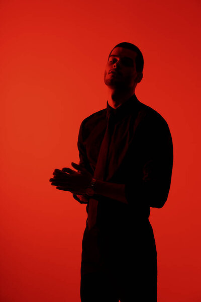 Silhouette of a young confident handsome businessman wearing black shirt in red light