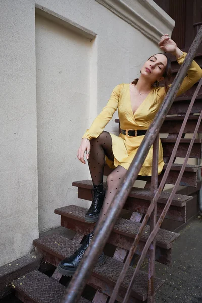 Uma jovem mulher moderna em vestido amarelo posando em escadas — Fotografia de Stock