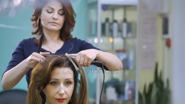 Parrucchiere utilizzando piastra su bei capelli donna nel salone di parrucchiere. Ondulazione arricciacapelli — Video Stock