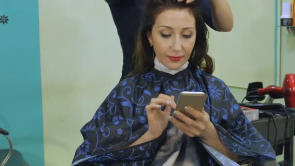 Estilo de cabelo menina bonita é um mestre Barbeiro. O modelo com o smartphone, online banking — Vídeo de Stock