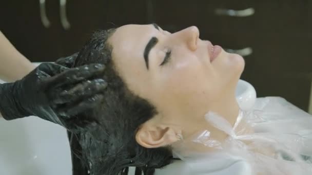 Barbería. cabeza, vista lateral. mujer lava la pintura con el pelo largo negro Chica bonita con una pintura en las cejas de los clientes . — Vídeo de stock