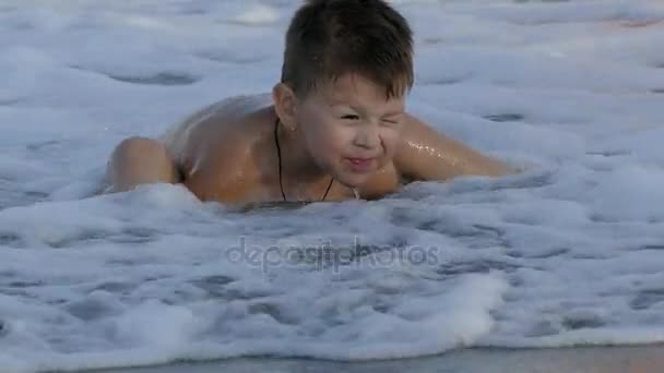 Carino piccolo bambino seduto sulla spiaggia e godendo le onde che giocano con la sabbia. Rallentatore — Video Stock