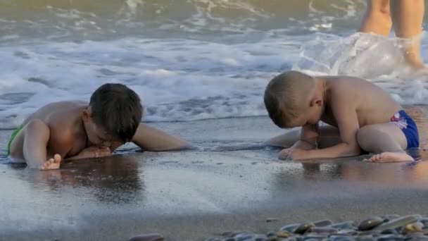 Милый малыш сидит на пляже и наслаждается волнами, играя с песком. Медленное движение — стоковое видео