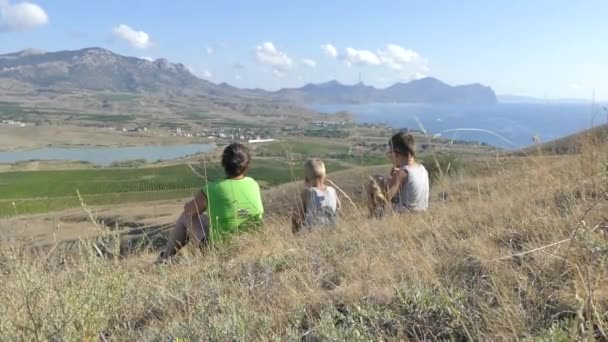 La familia en la cima de la colina mira al lago en el valle, en el mar, en las montañas, en la llanura con viñedos . — Vídeos de Stock