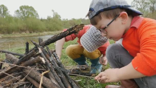 Två små pojkar gör en eld på de pittoreska stranden av floden. — Stockvideo