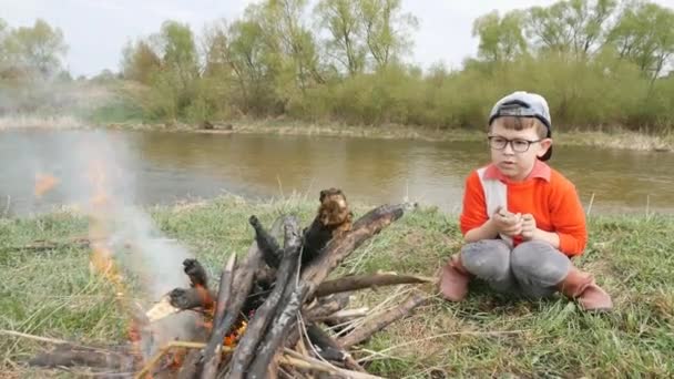 Špinavý malý kluk je obsazení hořící ohně na pozadí řeka na jaře — Stock video