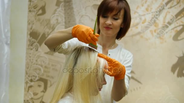 The hair stylist makes hair coloring, blonde, dyes the roots of the hair. — Stock Video