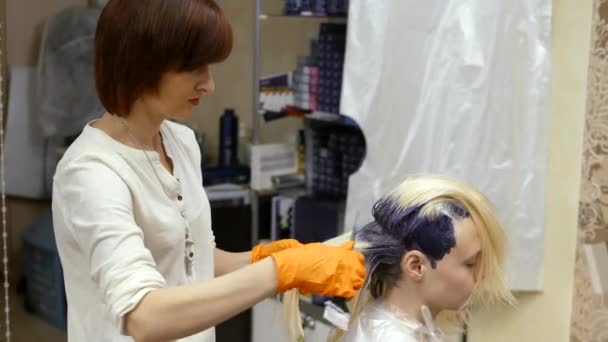 Волосся-стиліст робить колір волосся, блондинка, фарби волосся в синьому . — стокове відео