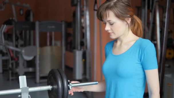 Hala sportowa. Dziewczyna jest trening na siłowni. umieszczenie naleśnik na pasku pasku — Wideo stockowe