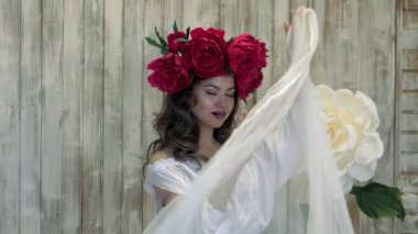 Kamera önünde poz kız. başında kırmızı peonies çelenk genç kadın, siyah uzun kıvırcık saçlı sığ omuzlarında iner..