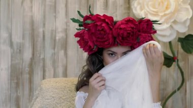 Kamera önünde poz kız. başında kırmızı peonies çelenk genç kadın, siyah uzun kıvırcık saçlı sığ omuzlarında iner..
