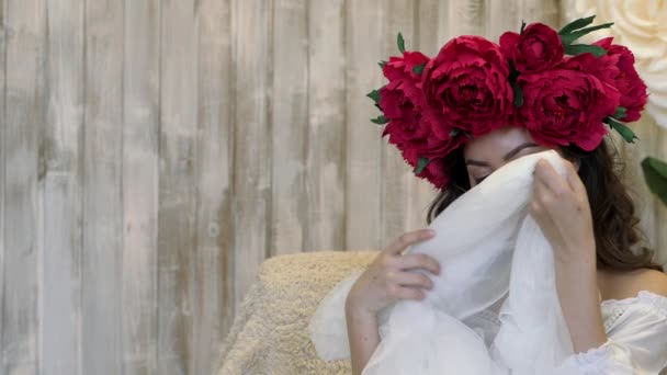 Girl posing in front of camera. young woman in a wreath of scarlet peonies on her head, dark long curly hair descends on the shallow shoulders. — Stock Video