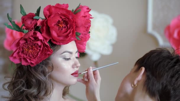 Make-up artiest stylist werkt met model. samenstelling van een jong meisje in een schoonheidssalon. Visagist die gebruik maakt van make-up op het gezicht van het model. De brunette vrouw zit terwijl de kunstenaar door middel van werkt de — Stockvideo