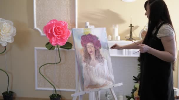 Kunstenaar trekt een portret uit de natuur. De kunstenaar trekt een portret uit de natuur. Zwevende focus van de camera, camera in beweging. Mooi model, met een krans van scarlet pioenrozen op zijn hoofd, die zich voordeed in zit — Stockvideo