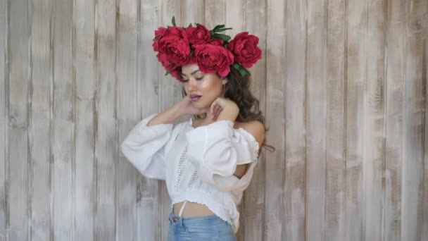 Girl posing in front of camera. young woman in a wreath of scarlet peonies on her head, dark long curly hair descends on the shallow shoulders. — Stock Video