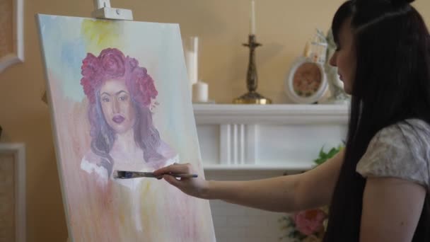 Artista disegna un ritratto dalla natura. L'artista disegna un ritratto dalla natura. Fuoco flottante della telecamera, telecamera in movimento. Bella modella, con una corona di peonie scarlatte in testa, in posa seduta in — Video Stock