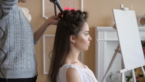 Artista de maquillaje estilista trabaja con modelo. peluquería hace el peinado del modelo. mujer está trabajando un estilista con las niñas de pelo largo. La peluquera hace rizos en el pelo liso de las niñas — Vídeos de Stock