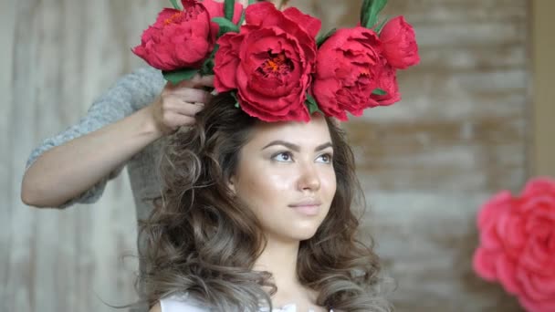 Makeup artist stylist works with model. A stylist dresses a wreath of red pions on the girls head model. — Stock Video