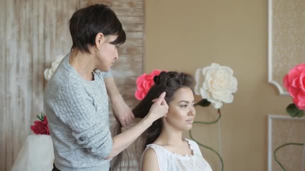 Truccatore stilista lavora con il modello. parrucchiere fa lo styling dei capelli del modello. donna sta lavorando un styler con le ragazze capelli lunghi. Il parrucchiere fa riccioli sui capelli lisci delle ragazze — Video Stock