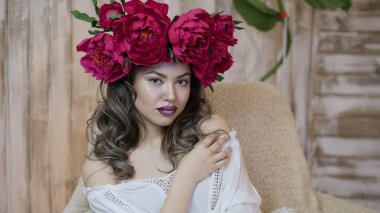 Kız model poz. başında kırmızı peonies çelenk genç bir kadın, siyah uzun kıvırcık saçlı küçük omuzlarında iner.